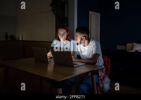 Young interracial couple looking at laptop discussing online family business, working late at home Stock Photo