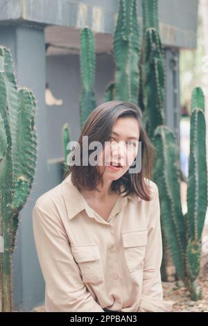 A woman wearing a brown shirt sitting with a cactus Stock Photo