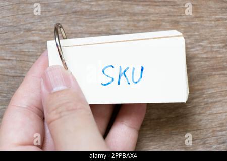 Hand hold flash card with handwriting in word SKU (Abbreviation of stock keeping unit) on wood background Stock Photo