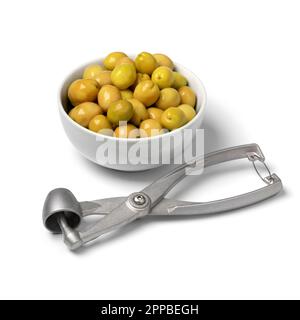 Bowl with green Turkish olives close up  and a metal olive pitter and pitted olive in front isolated on white background Stock Photo