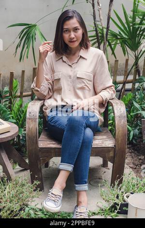 Woman sitting on a wooden chair in the backyard Stock Photo