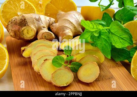 Lemons, ginger and mint leaves. Lemon halves, slices of ginger and mint leaves on a wooden board. Stock Photo