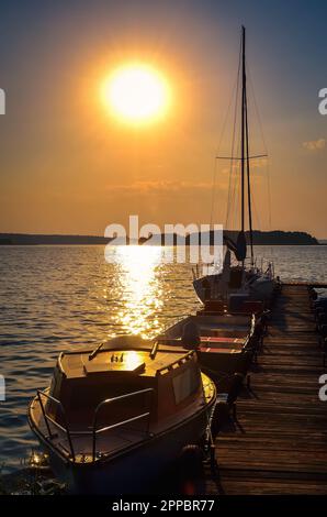 Sailing yacht and jetty in the beautiful lake. Empty wooden jetty with moored boats on the lake shore at the sunrise in Mazury region, Poland. Stock Photo