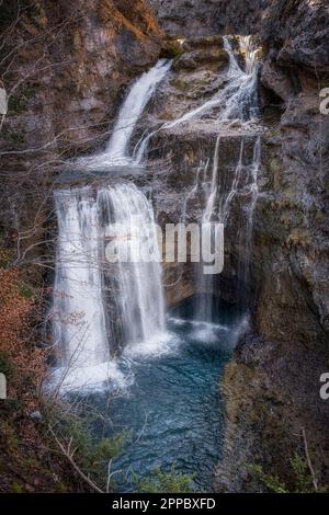 waterfall the Cave in the heart of the National Park of Ordesa and Monte Perdido, set in a rocky canyon, branches and small tree with autumn colored l Stock Photo