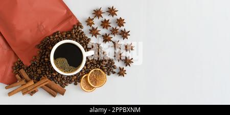 White cup of coffee top view. Coffee beans and packing bag. An invigorating drink in the morning for breakfast. Food background. Copy space banner. Anise stars, cinnamon sticks and dried orange. Stock Photo