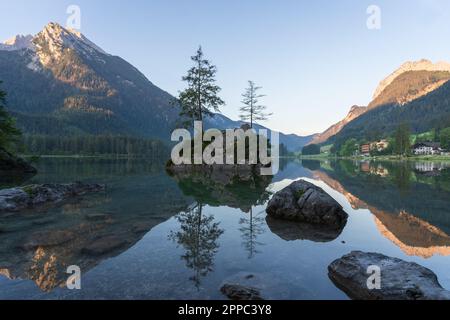 Crystal clear alpine tarn with rocky islands with tree on them during sunrise, Hintersee, Germany Stock Photo