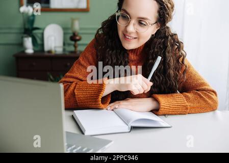 Young smiling pretty woman student using laptop elearning or remote working at home office using laptop computer watching webinar, learning web course Stock Photo