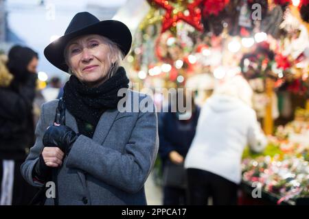 Positive elderly woman in festive mood walking on street Christmas fair Stock Photo