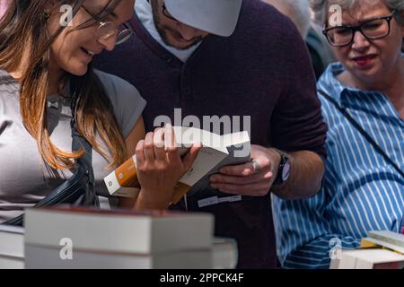 Barcelona, Spain. 23rd Apr, 2023. A couple examines a book in one of the stalls on La Rambla. Catalonia annually celebrates the Day of Sant Jordi on April 23, the traditional book and rose festival. The streets are full of stalls selling books and roses. Credit: SOPA Images Limited/Alamy Live News Stock Photo