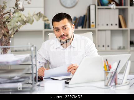Positive man bookkeeper doing paperwork in office Stock Photo