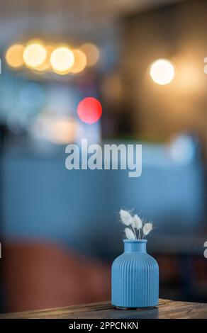 Small blue minimalistic ceramic vase on a table at a cafe with dried flowers Stock Photo