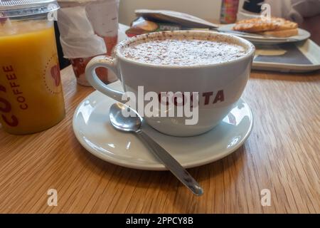 A mug of cappuccino coffee in a mug on a sauce at a Costa Coffee cafe. Stock Photo