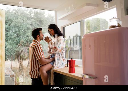 Man looking at woman sitting on kitchen counter at home Stock Photo