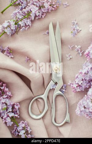 Scissors and lilac flowers on linen fabric Stock Photo