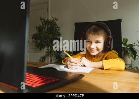 Smiling boy wearing headset studying online through laptop at home Stock Photo