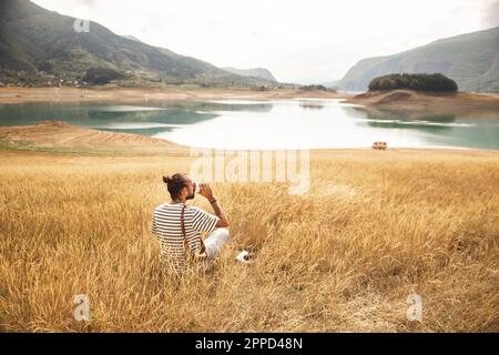 Man drinking coffee sitting in front of Rama Lake Stock Photo