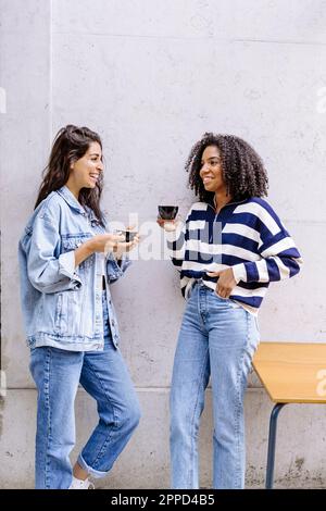 Happy friends standing with coffee cups leaning on wall Stock Photo
