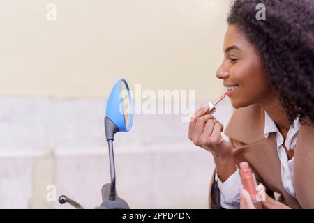 Young woman applying lipstick looking in mirror Stock Photo