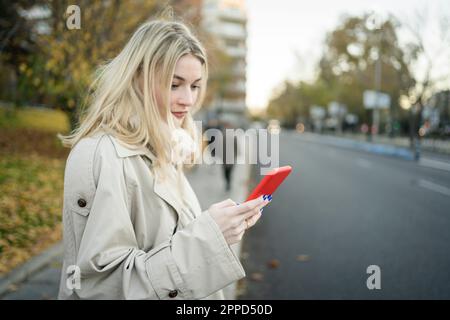 Blond woman using smart phone at sidewalk Stock Photo