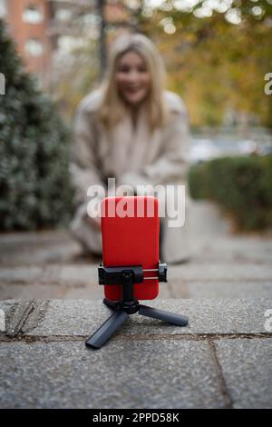 Smart phone mounted on tripod with woman vlogging in background Stock Photo