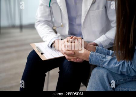 Doctor holding hands and consoling patient in clinic Stock Photo