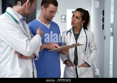 Doctor discussing with colleagues over medical record in clinic Stock Photo