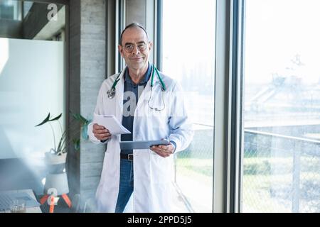 Smiling mature doctor holding prescription and tablet PC Stock Photo