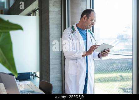 Doctor using tablet computer standing by window Stock Photo