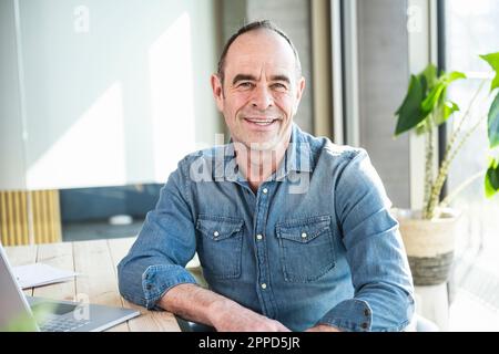 Happy mature businessman sitting at desk in office Stock Photo