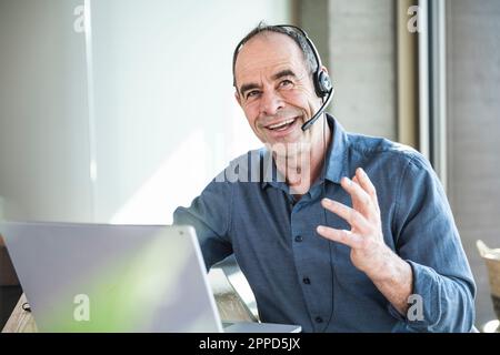 Happy mature businessman wearing headset discussing over laptop in office Stock Photo