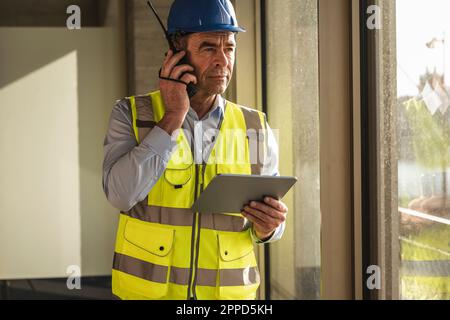 Engineer using walkie talkie standing with tablet PC in office Stock Photo