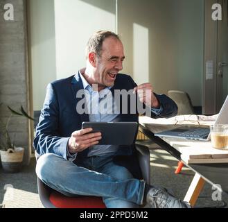 Happy mature businessman with clenched fist looking at laptop in office Stock Photo