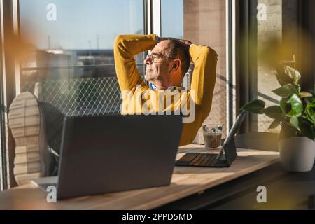 Contemplative businessman sitting with hands behind head at desk in office Stock Photo