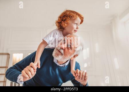 Grandfather giving piggyback ride to grandson at home Stock Photo