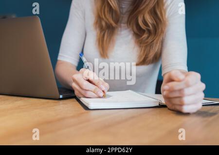 Freelancer taking down notes in diary at desk in home office Stock Photo