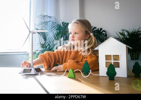 Girl operating with wind turbine model for green toy house on table Stock Photo