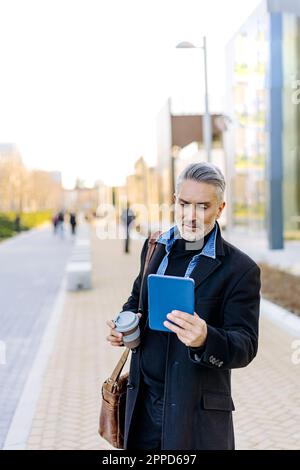 Businessman using tablet PC standing at footpath Stock Photo