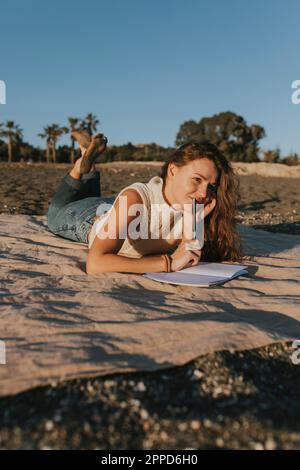 Thoughtful woman lying on blanket with note pad Stock Photo