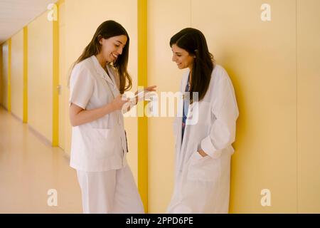 Smiling doctors sharing smart phone standing in corridor Stock Photo