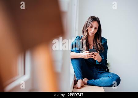 Young businesswoman text messaging through smart phone at home Stock Photo