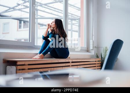 Thoughtful young woman looking through window Stock Photo