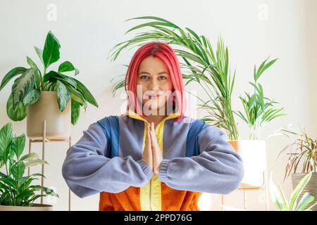 Smiling woman with prayer pose in front of wall at home Stock Photo