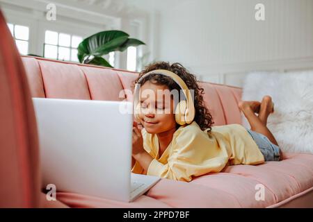 Girl wearing wireless headphones studying on laptop at home Stock Photo