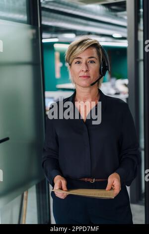 Smiling businesswoman wearing headset standing at door Stock Photo