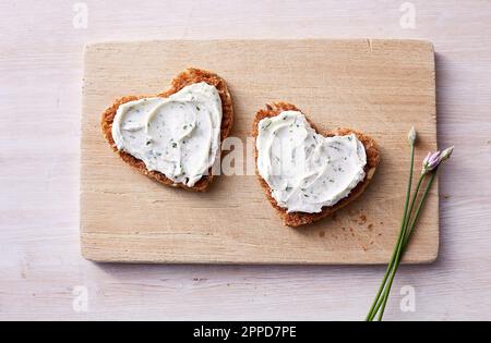 Two heart shaped sandwiches with cream cheese and chives on cutting board Stock Photo