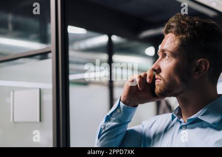 Thoughtful young businessman talking on smart phone in office Stock Photo