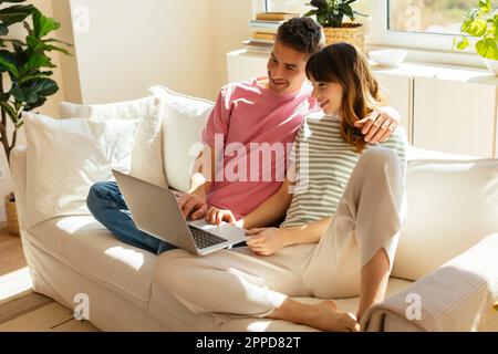 Smiling couple using laptop sitting on sofa at home Stock Photo