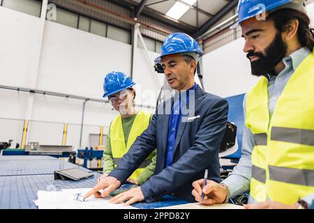 Mature engineers having discussion over blueprint in industry Stock Photo