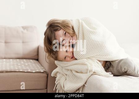Happy mother and son wrapped in blanket on sofa at home Stock Photo