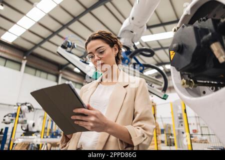 Young engineer using tablet PC in front of robotic arm Stock Photo